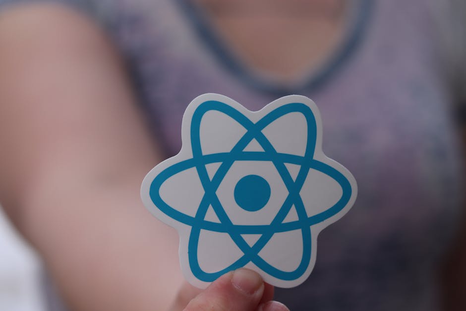 A person holding a white card with a blue stylized atomic symbol on it, featuring interconnected loops and a central dot, in front of a blurred background of a person wearing a purple top and a grey n